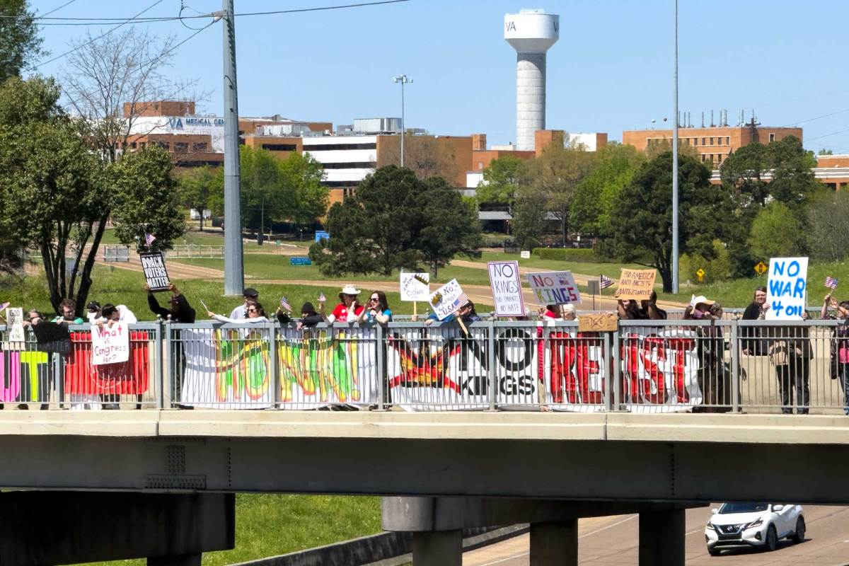 A bridge over the interstate is lined with protestors holding signs that read 'HONK!' 'NO KINGS' 'RESIST'