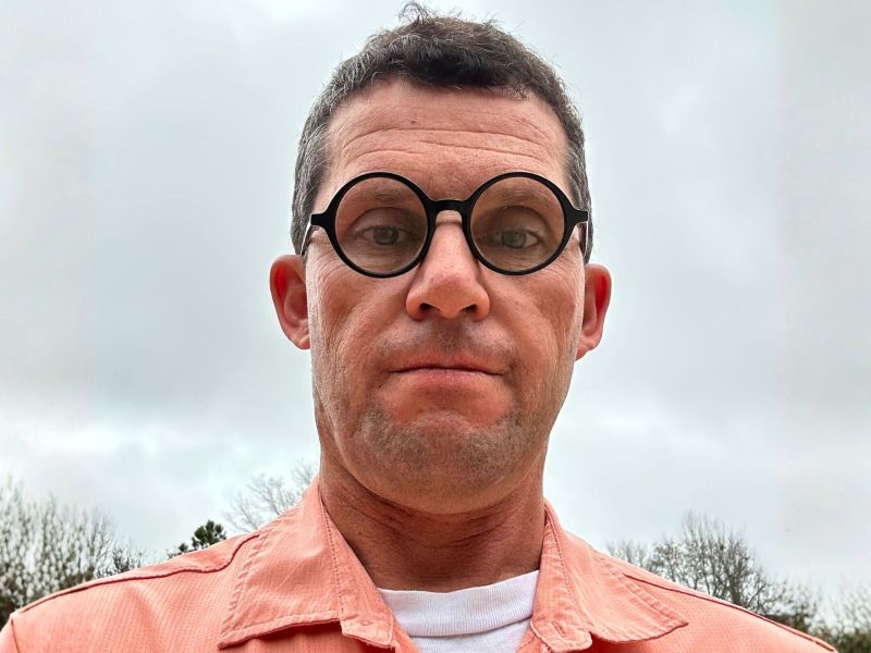 Paul Blackman wearing round black glasses and an orange shirt