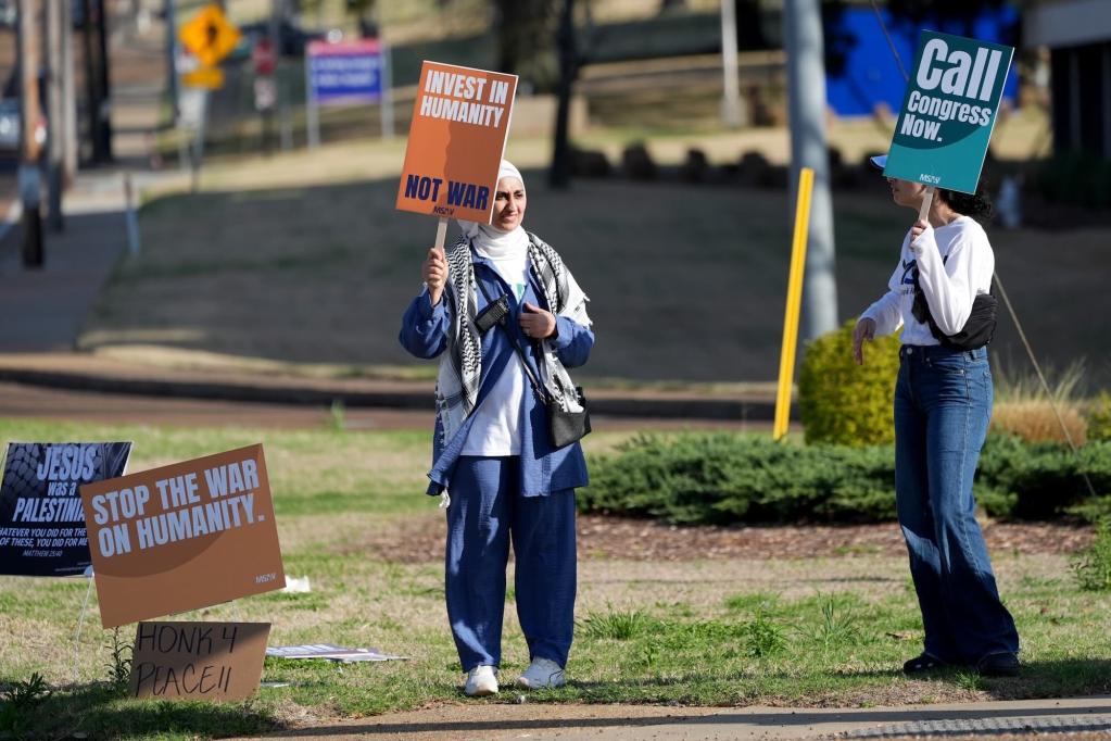 Protestors hold signs on the roadside reading 'Invest in Humanity' and 'Call Congress Now'