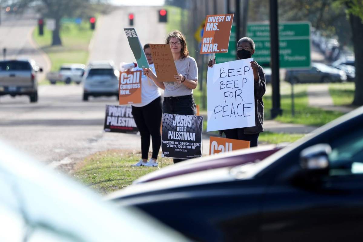 Protestors hold signs by the roadside that read 'Invest in MS' "Beep Beep for Peace'