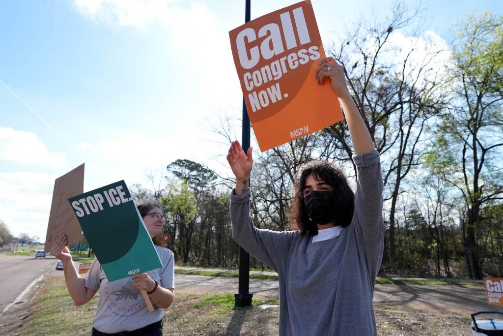 Two people hold signs on the roadside that reads 'Call Congress Now' and "Stop ICE'