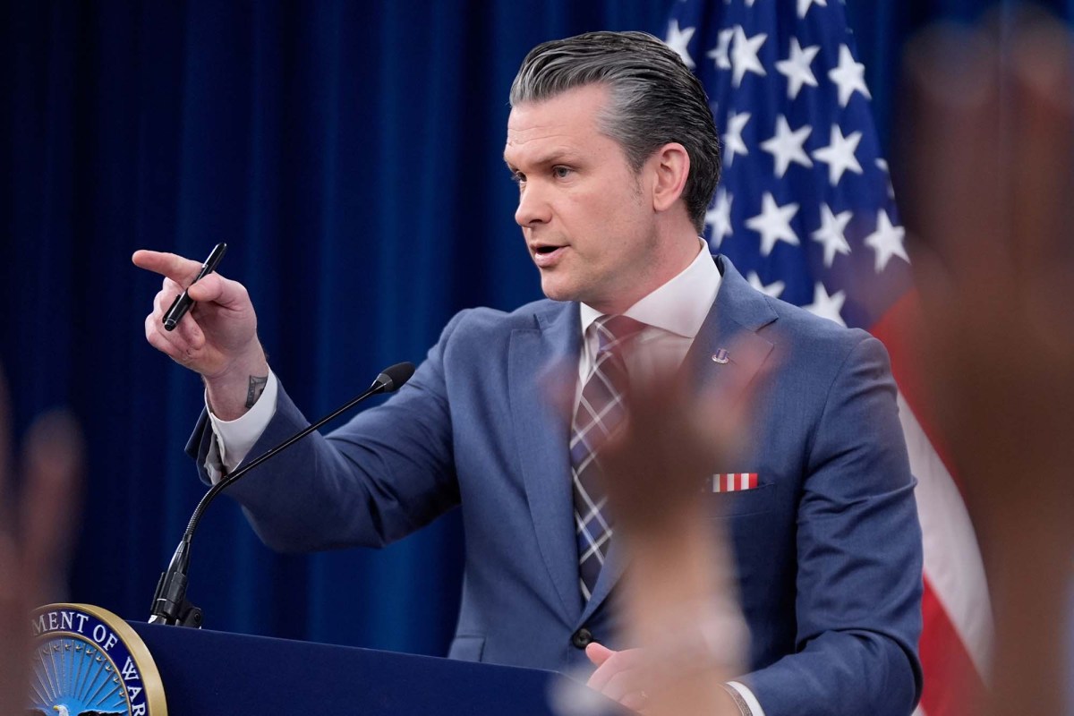 Pete Hegseth standing at a podium and pointing while he speaks