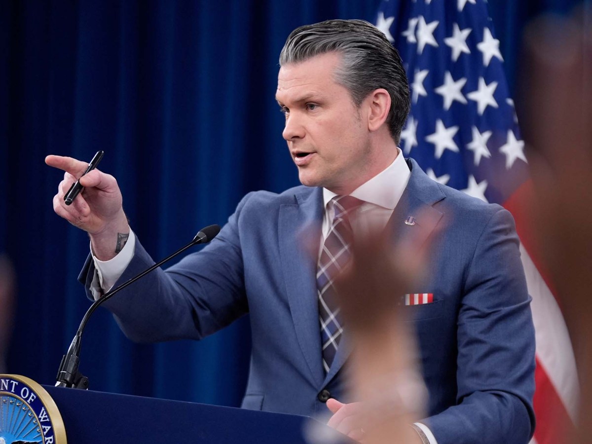 Pete Hegseth standing at a podium and pointing while he speaks