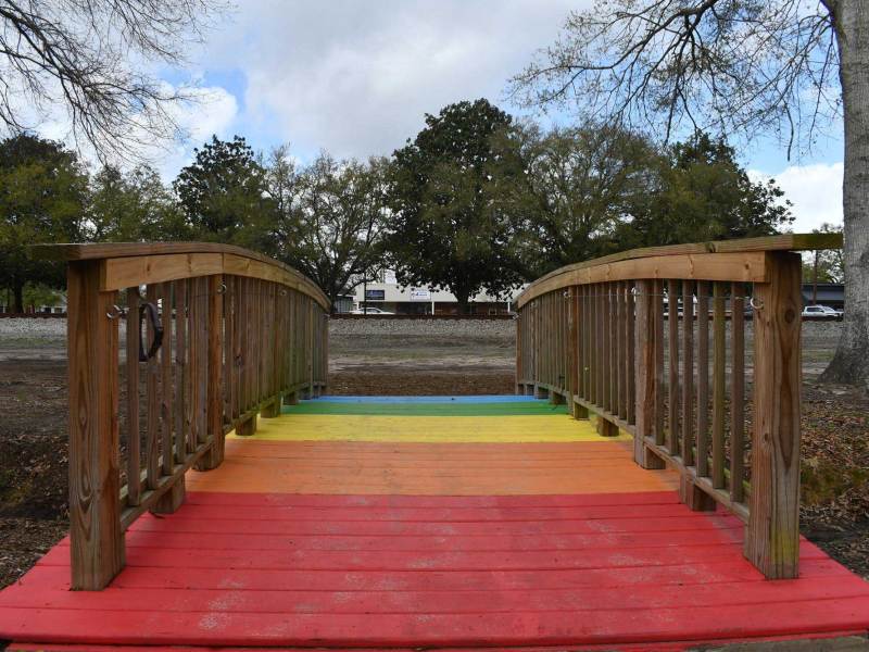 A small wooden bridge painted in rainbow colors crosses a shallow drainage ditch in Shay Park.