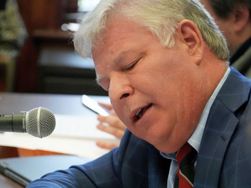A closeup of Rob Roberson II leaning and speaking into a mic at a committee