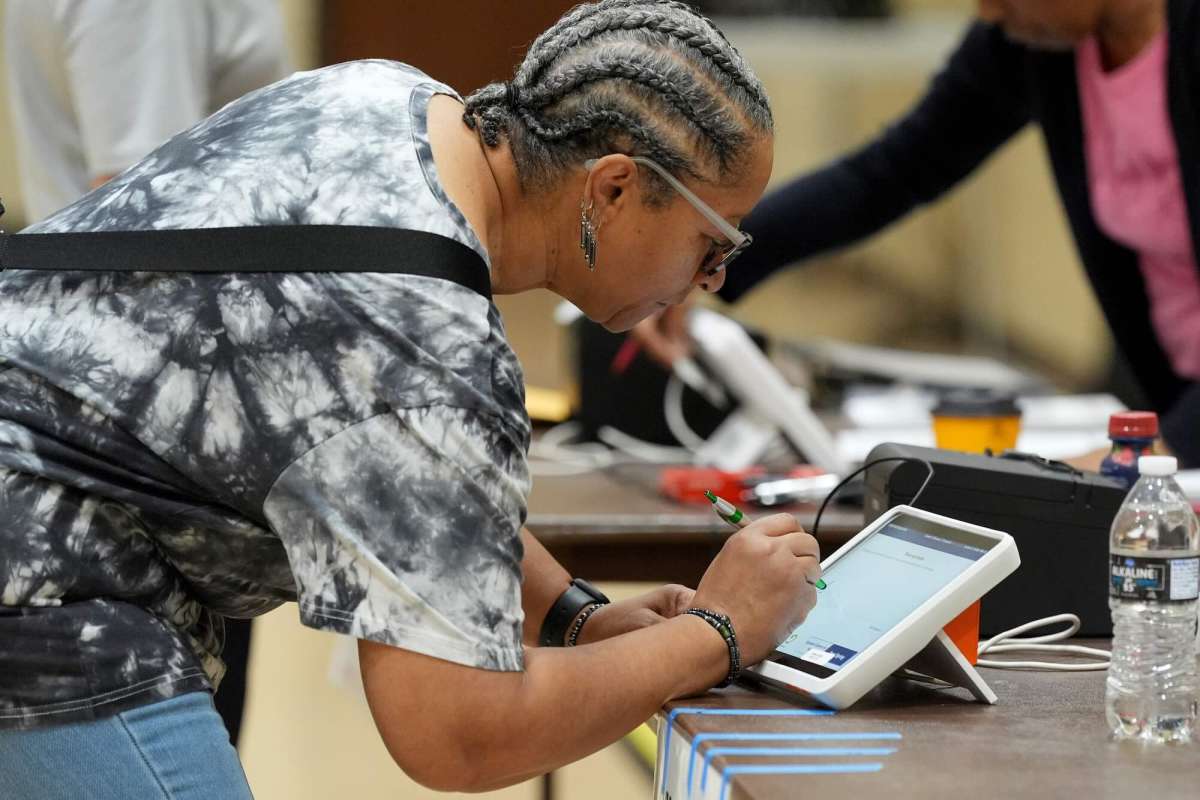A woman leans over a table and signs an electronic form prior to voting.