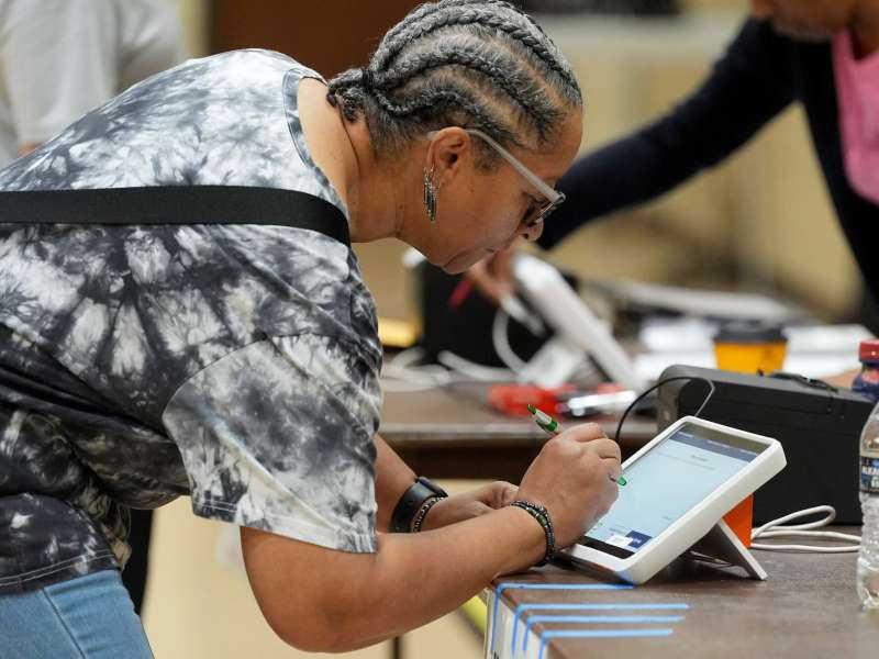 A woman leans over a table and signs an electronic form prior to voting.