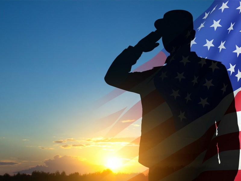 A silhouette of a man in military uniform saluting with the American flag in the background.