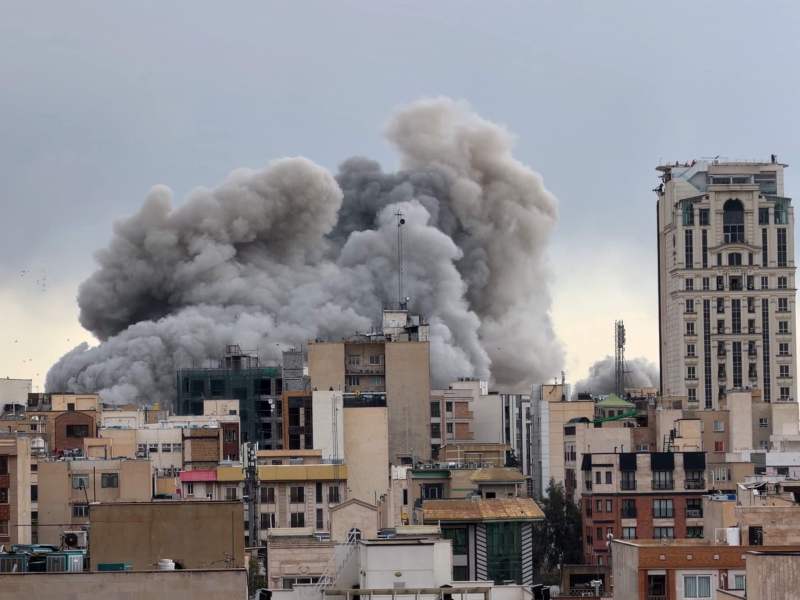 A large plume of smoke from a bombing rises from a cityscape