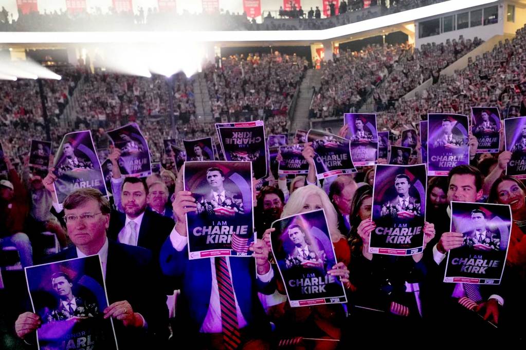 A large venue full of people including Tate Reeves holding up signs that say 'I am Charlie Kirk'