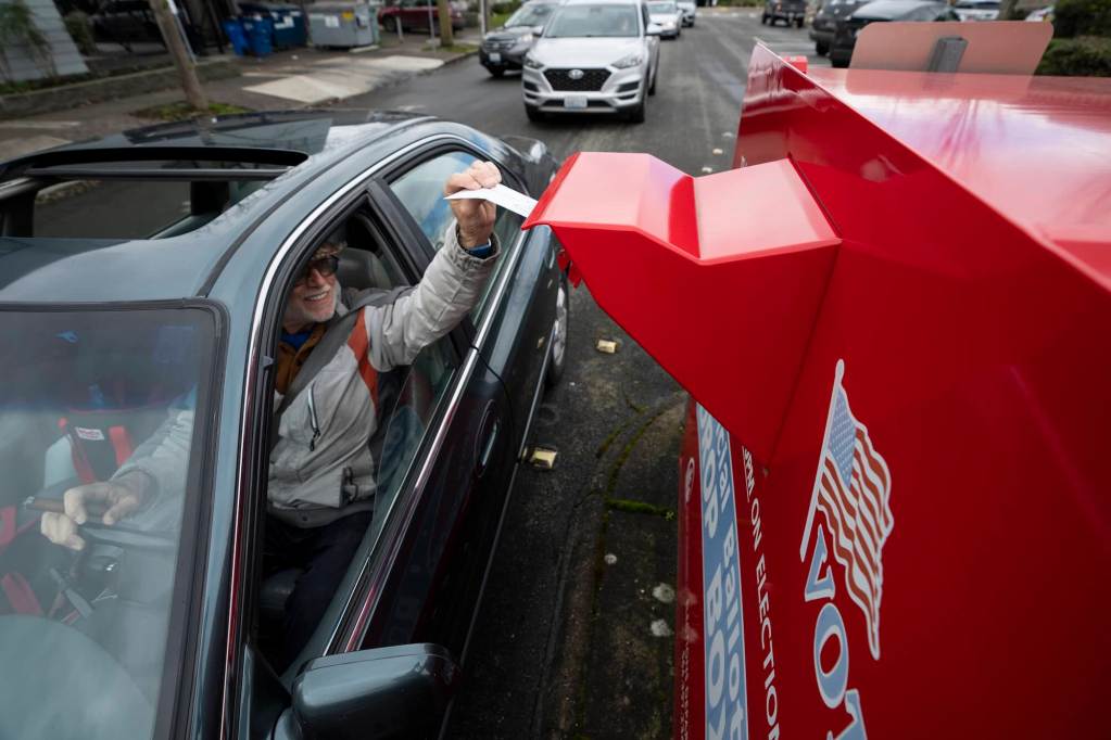 A person seen driving up and inserting a ballot into a red voter box on the roadside