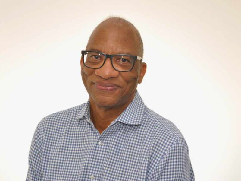 A man wearing glasses and a blue checkered shirt against a white background.
