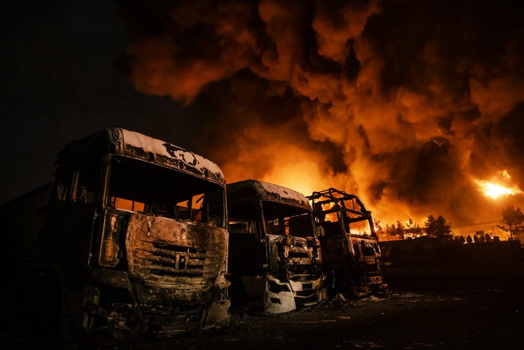 Thick smoke and flames over a row of burned out trucks at night