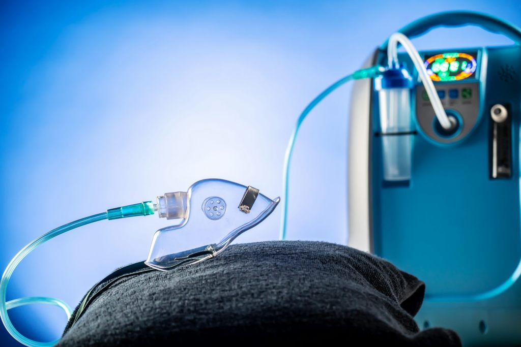 An oxygen mask displayed on a pillow. The mask is connected to a machine in the background.