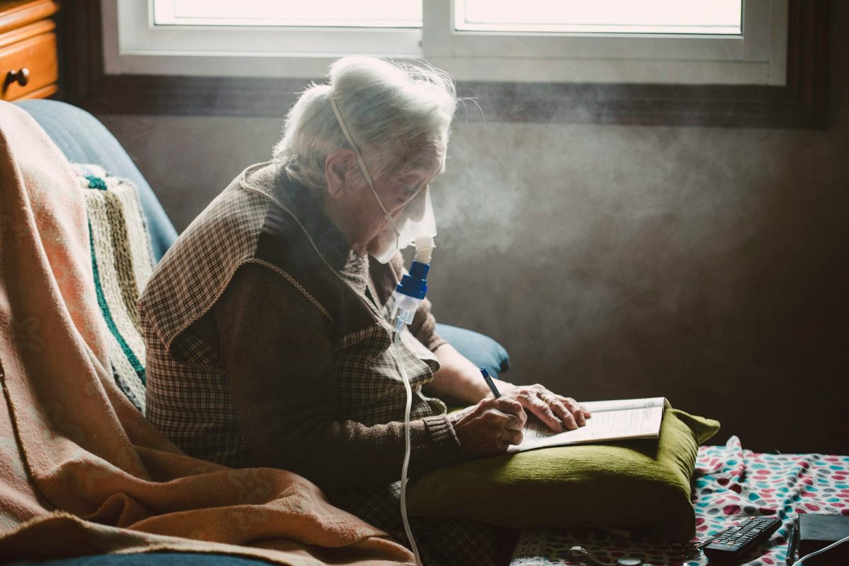 An elderly person seated in a chair wearing an oxygen mask.