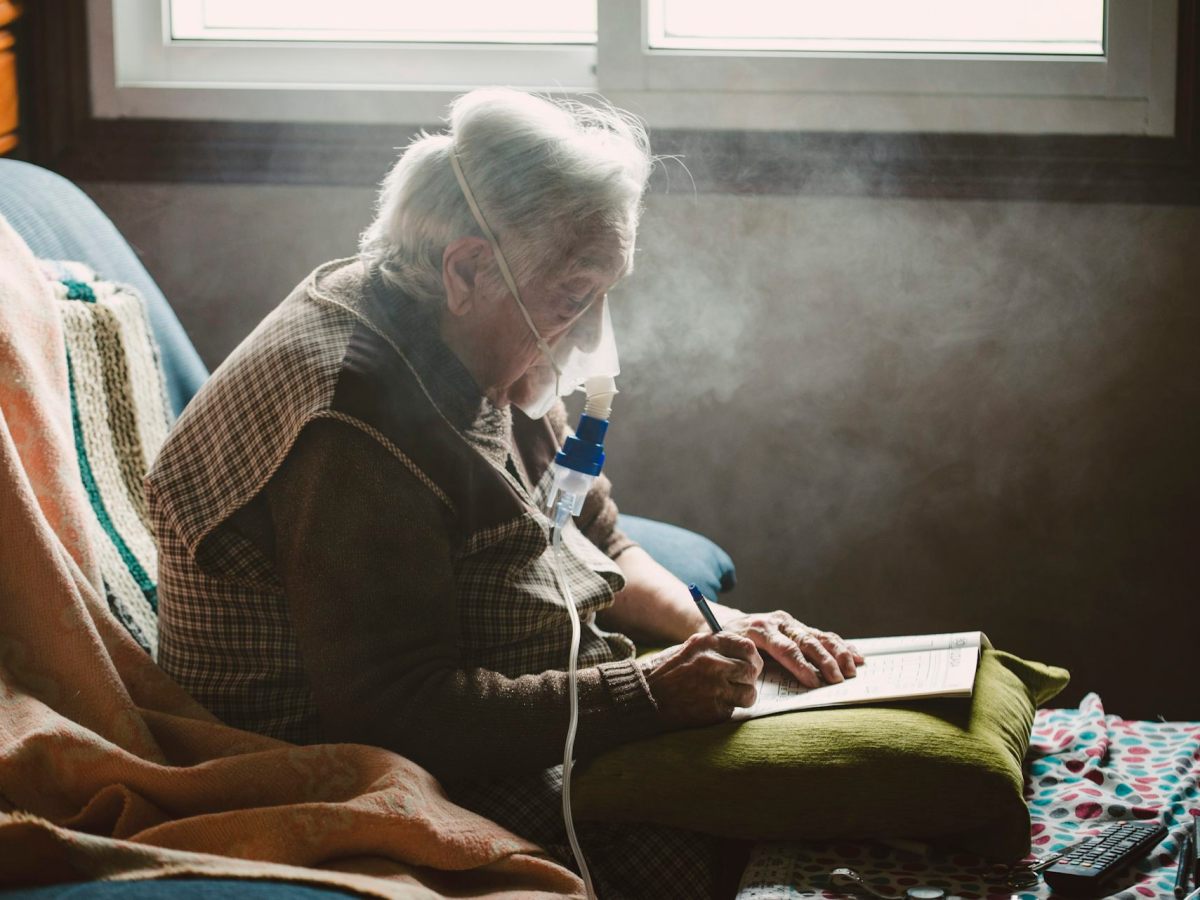An elderly person seated in a chair wearing an oxygen mask.