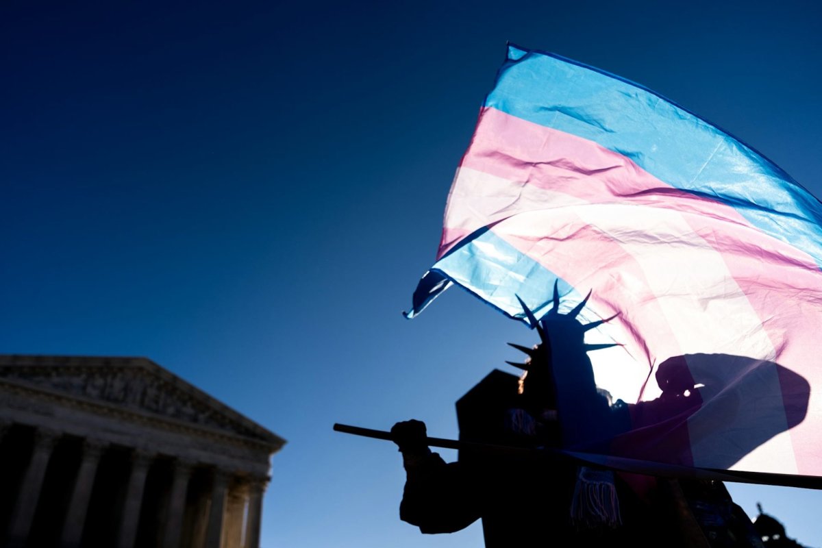 The silhouette of a protestor wearing a Statue of Liberty hat and waving the trans flag