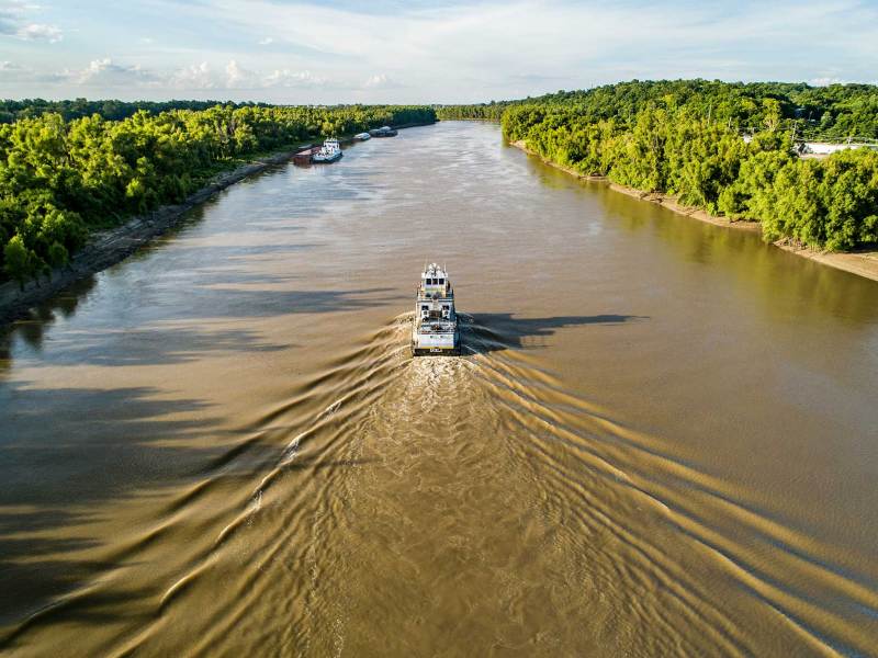 A boat traveling up a brown river cutting through a forest