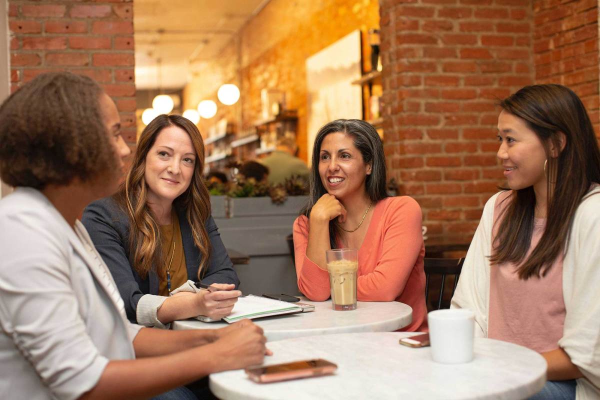 Four women sit around a table in a coffee shop, holding a meeting