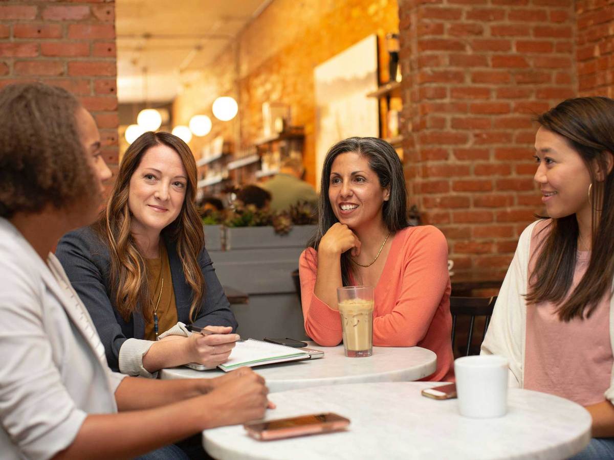 Four women sit around a table in a coffee shop, holding a meeting