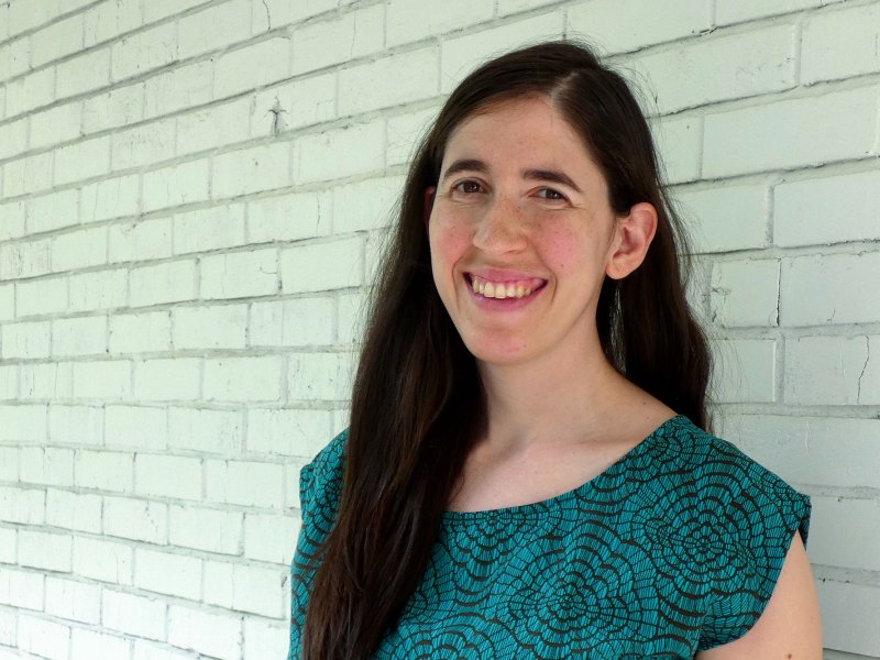 A closeup of a person with long brown hair standing in front of a brick wall
