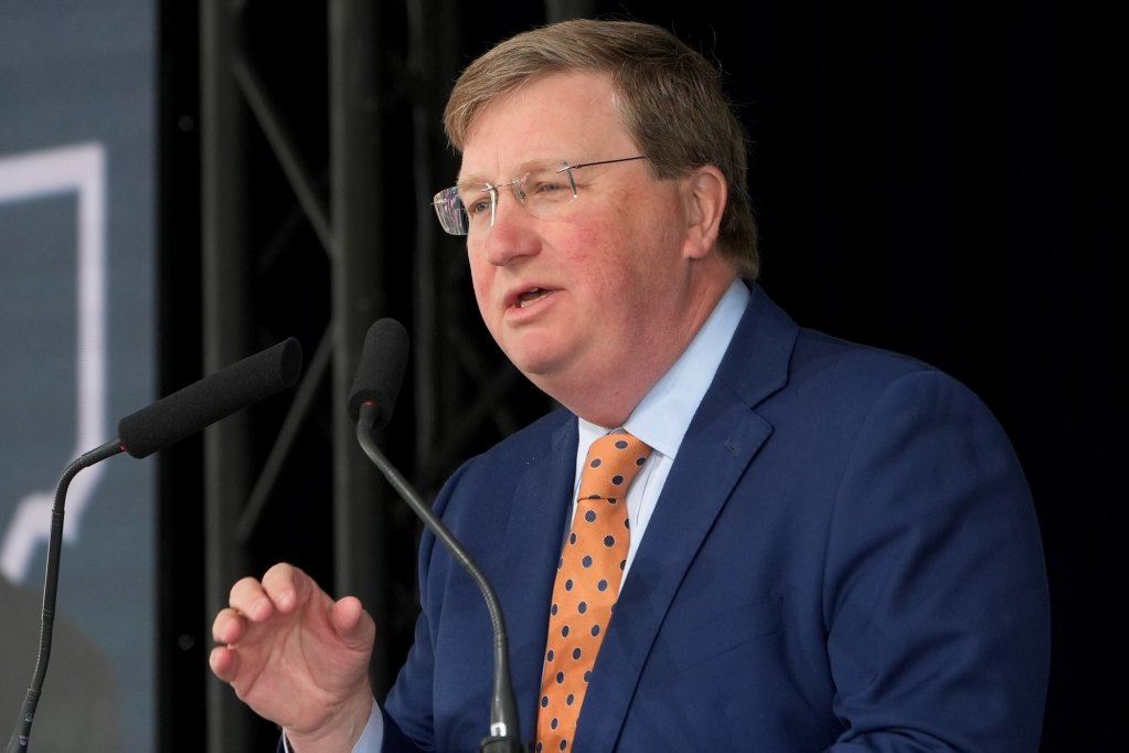 Tate Reeves, in a blue suit and gold tie, speaks at an Amazon press conference