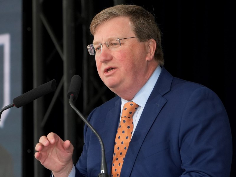 Tate Reeves, in a blue suit and gold tie, speaks at an Amazon press conference