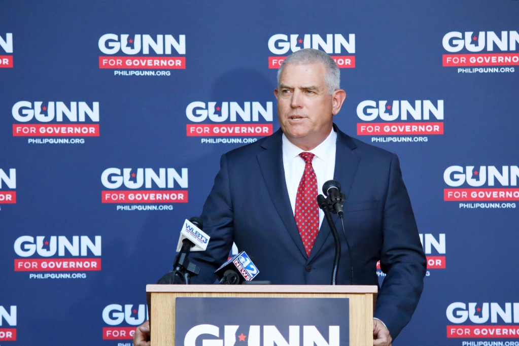Philip Gunn speaks at a podium in front of a wall covered in repeating logos that reads Gunn for Governor