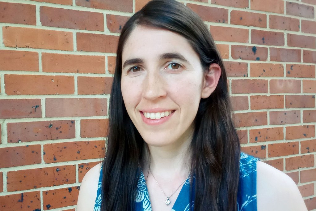 A closeup of a person with long brown hair standing in front of a brick wall