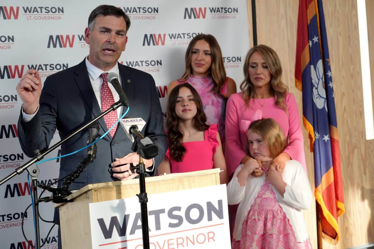 Michael Watson speaks at a press conference with his family beside him, all standing in front of a wall covered with MW logos that read Watson Lt. Governor