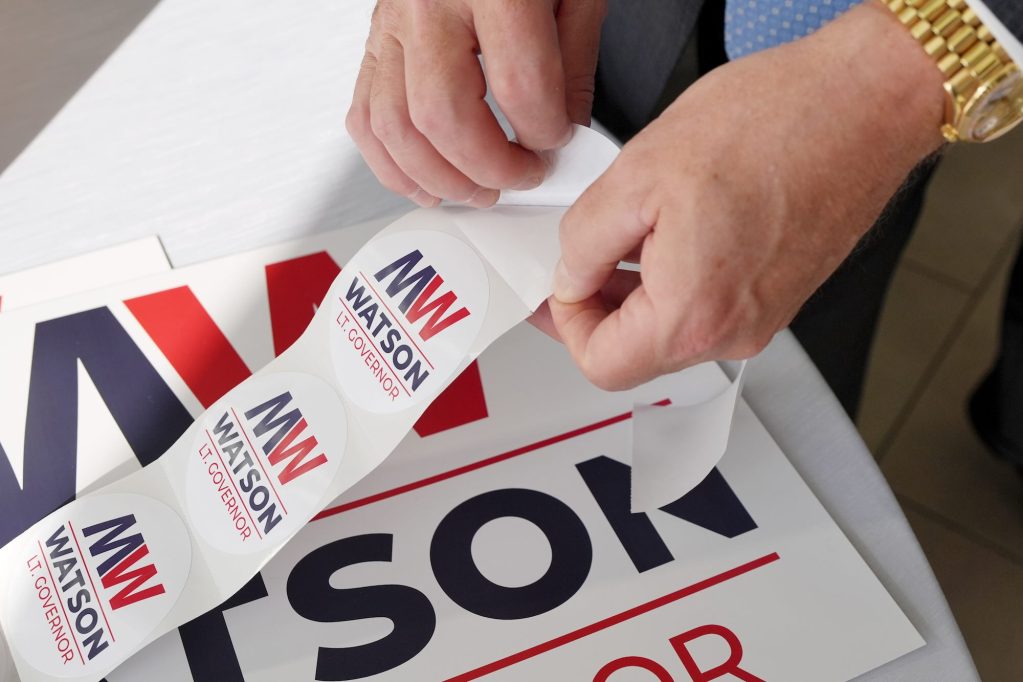 A person removes stickers that say 'MW Watson Lt. Governor' from a long sheet