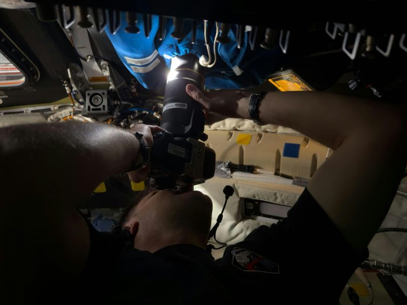 A man inside a spacecraft, pressing a camera against a window to take a photo.