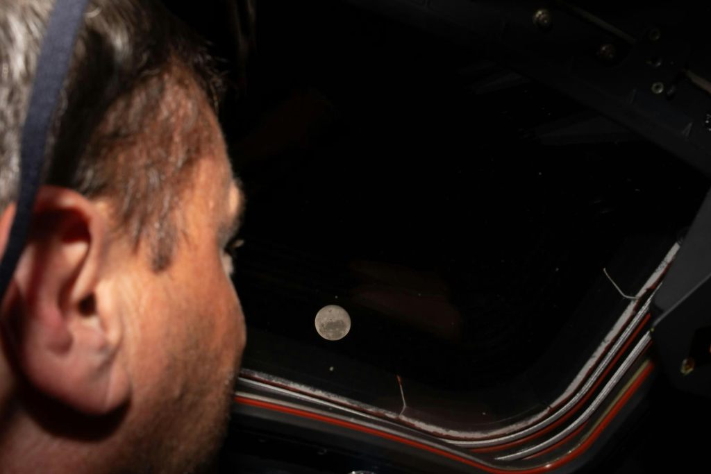 An astronaut looking out the window of the Orion spacecraft, where the full moon is visible in space
