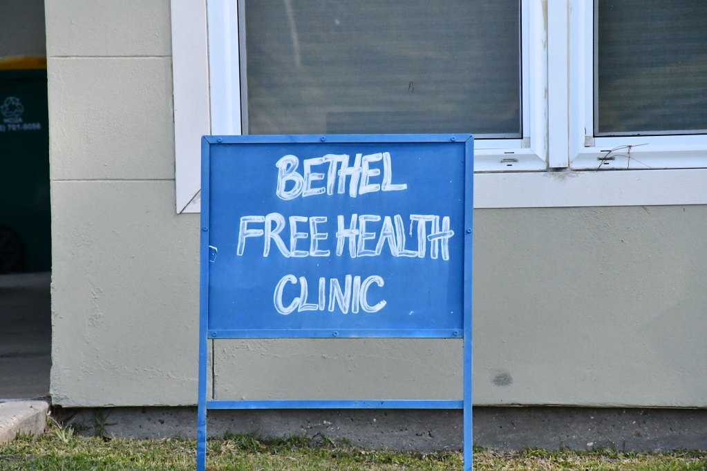 A blue hand-painted sign reading “Bethel Free Health Clinic.”
