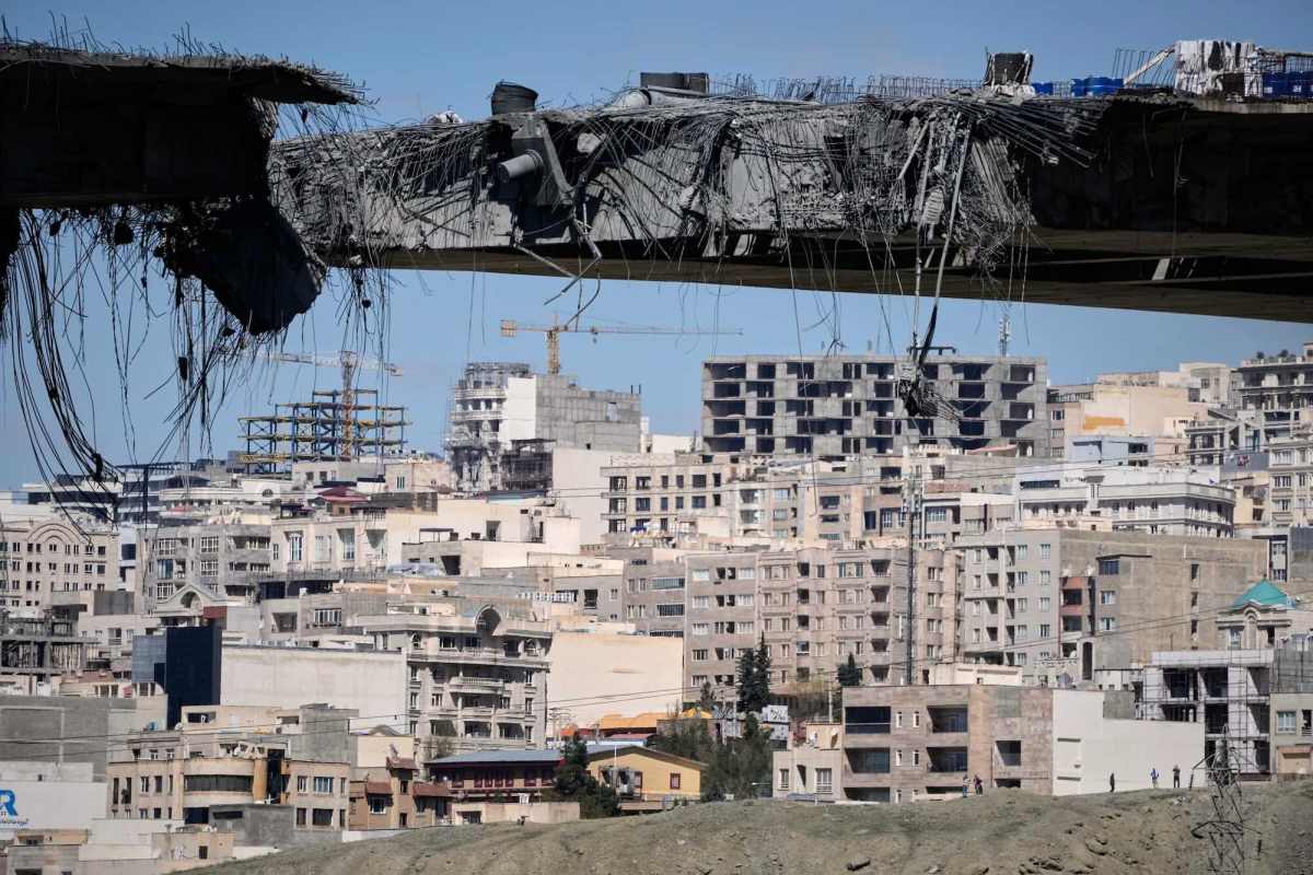 A damaged bridge with a damaged cityscape in the background.
