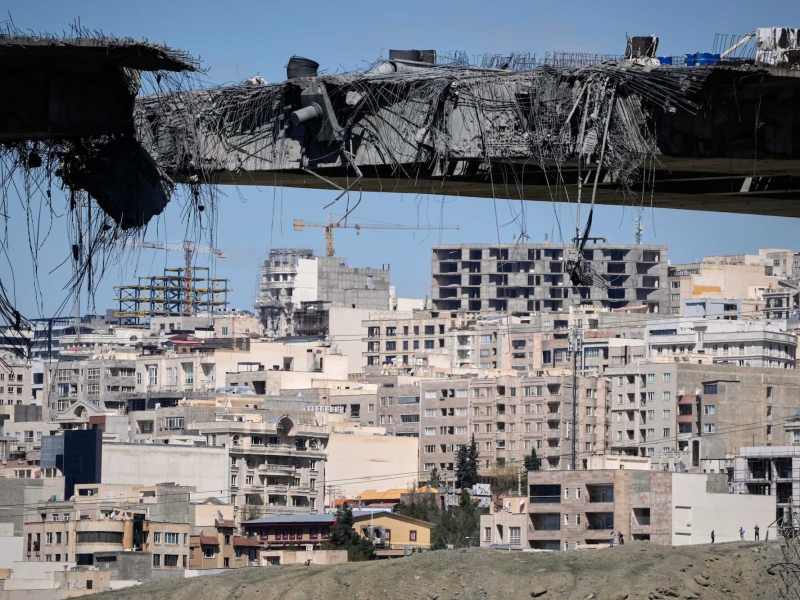 A damaged bridge with a damaged cityscape in the background.