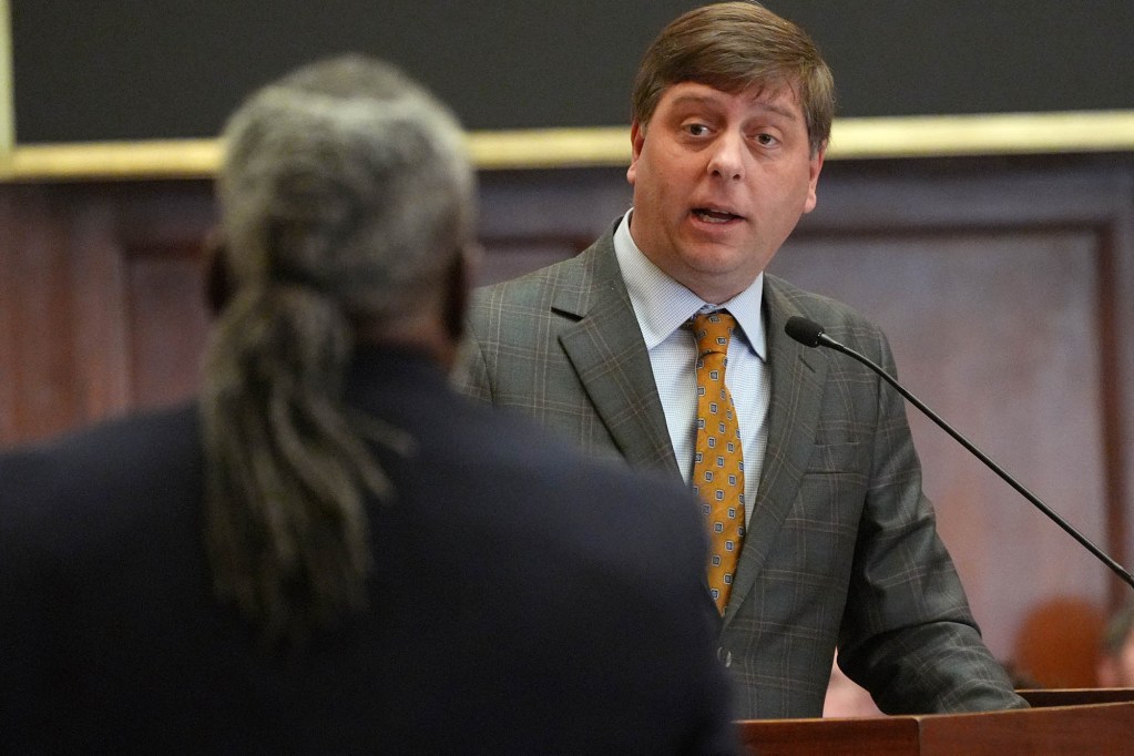 Clay Deweese, at a podium, speaking to another state representative at a meeting
