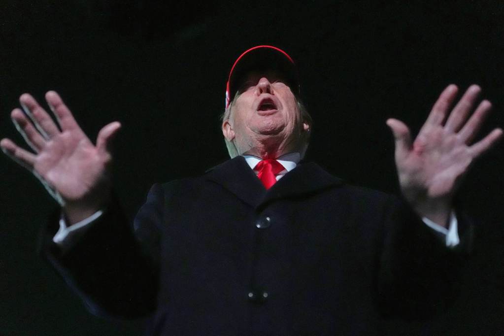 Donald trump in suit and red cap, speaking with hands spread out, as seen from a lower angle