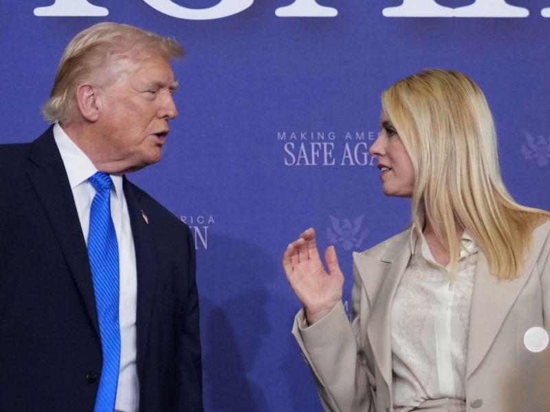 Donald Trump, on the left, speaks to Pam Bondi, on the right, at an event with signs that read 'Making America Safe Again'