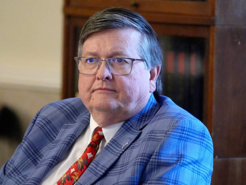 Dan Edney seen seated in an office wearing a plaid blue suit and red tie