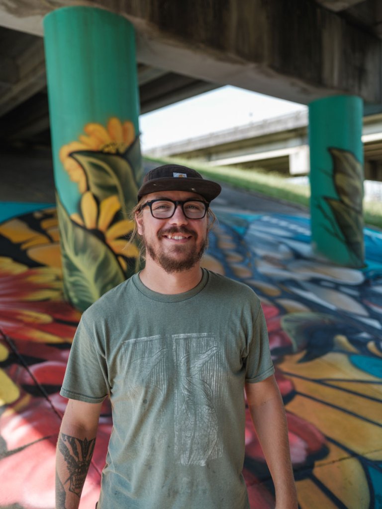 A man stands in front of the floral mural he painted under an interstate underpass