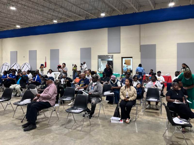 Numerous people seated in chairs inside a building.