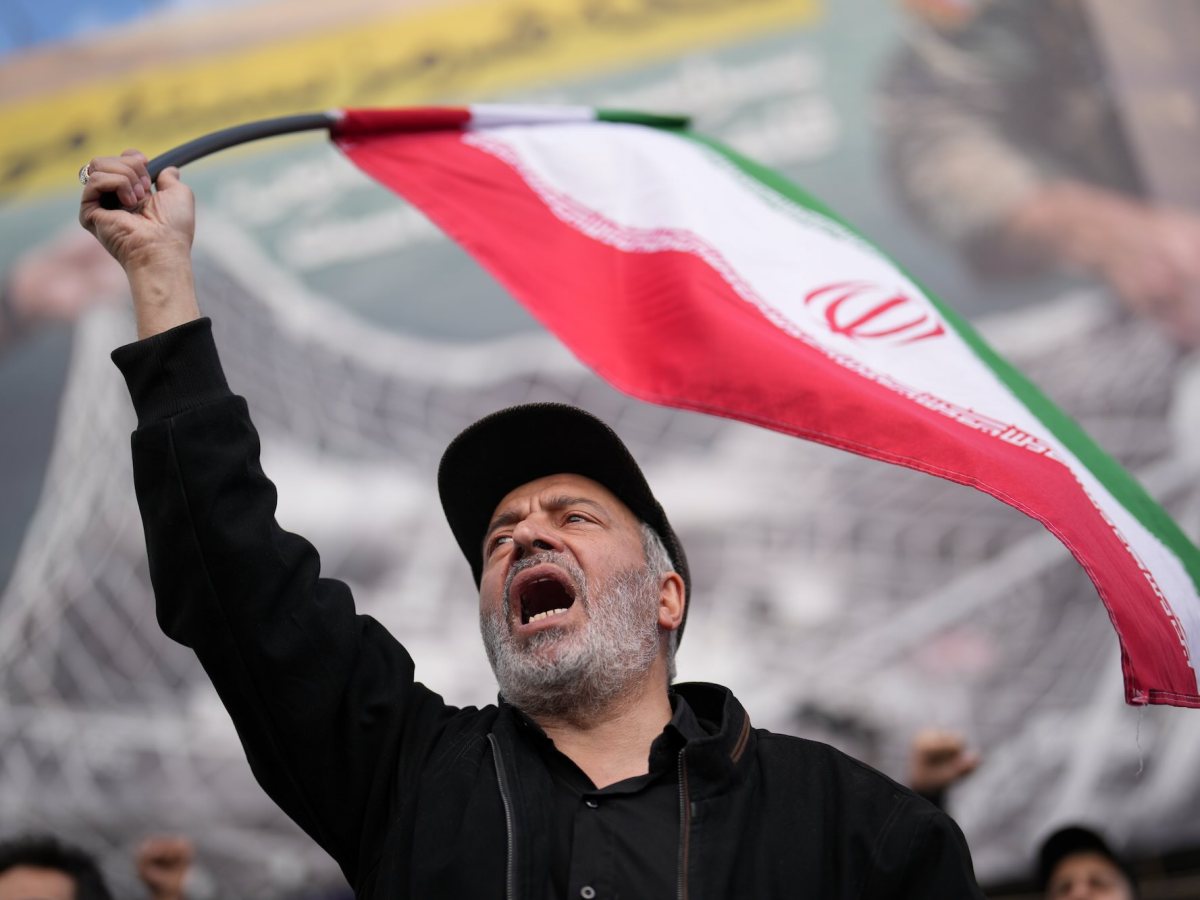 A man wearing a baseball cap and waving an Iranian flag