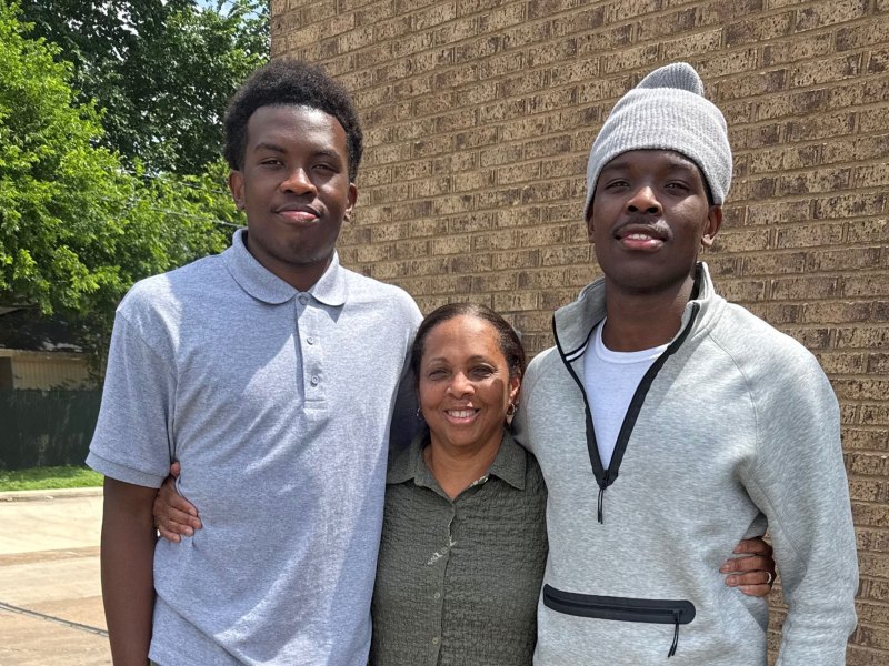 A woman smiles with her arms around two male teens who are standing on either side of her
