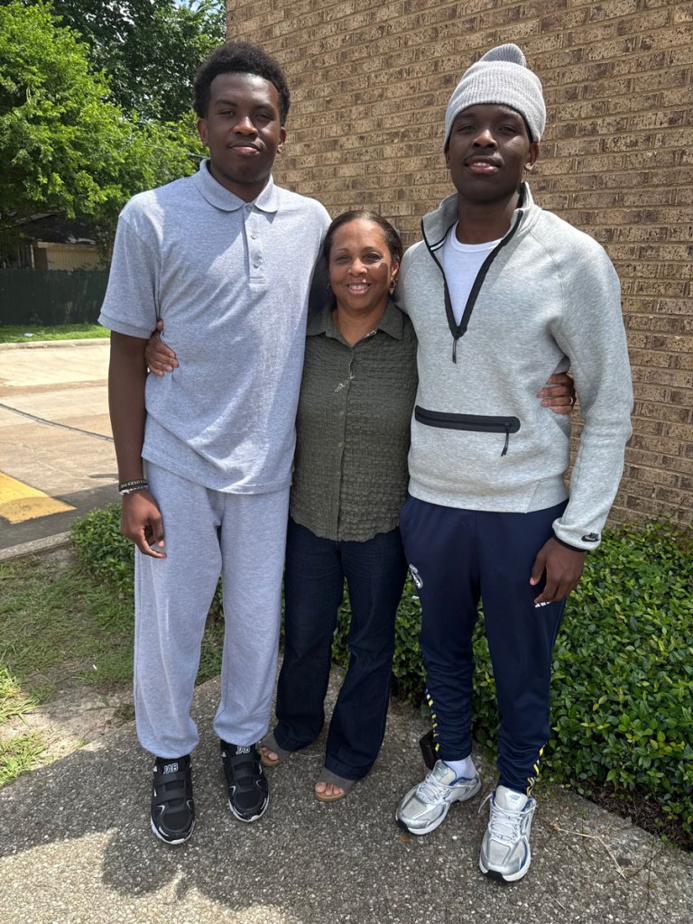 A woman smiles with her arms around two male teens who are standing on either side of her