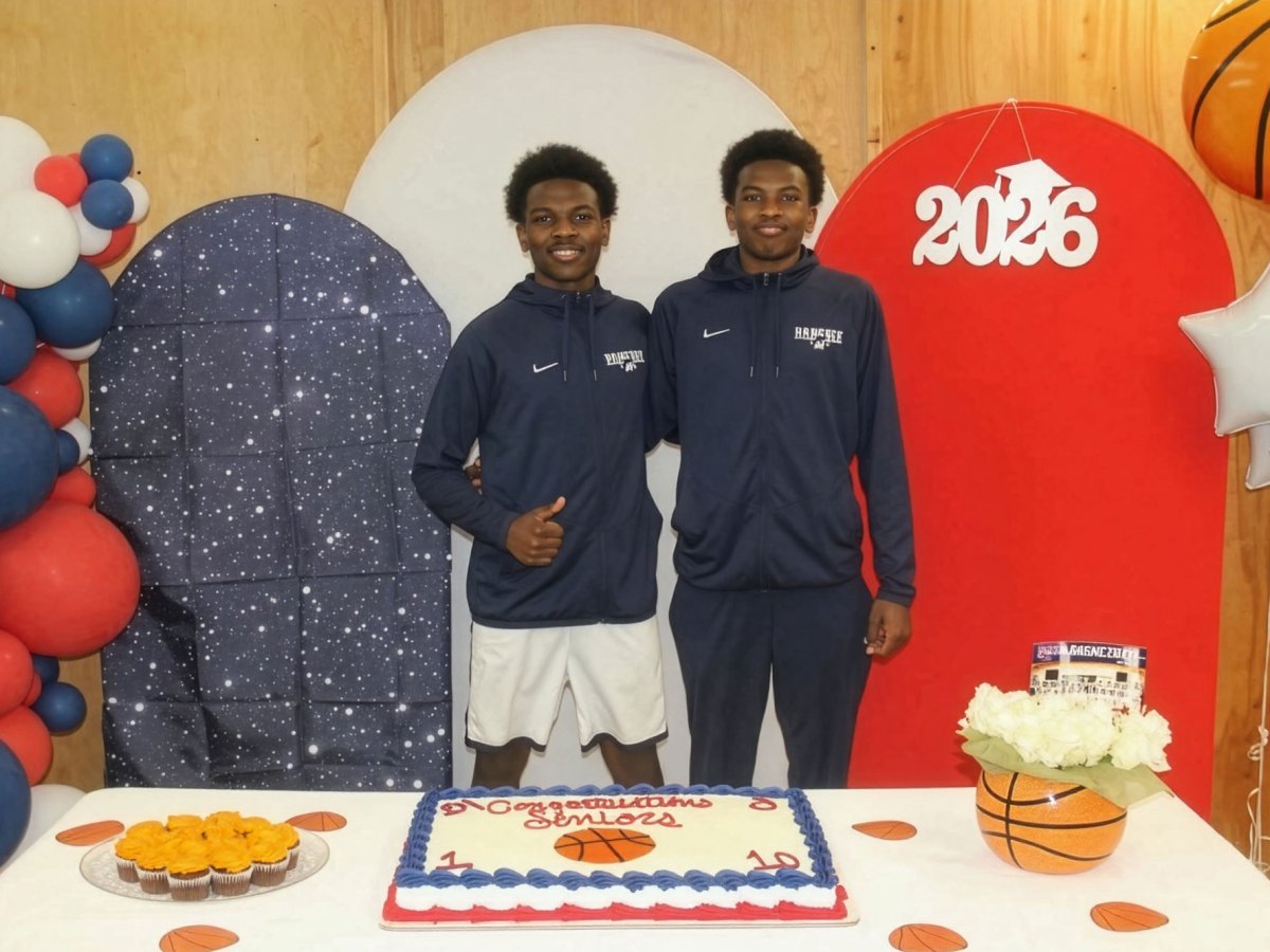 Two brothers in matching jackets pose surrounded blue red and white balloons, behind a table with a cake that says Congratulations Seniors