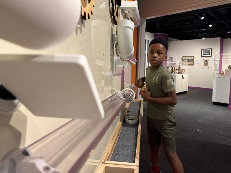 A young boy standing near a wall with interactive displays in a museum