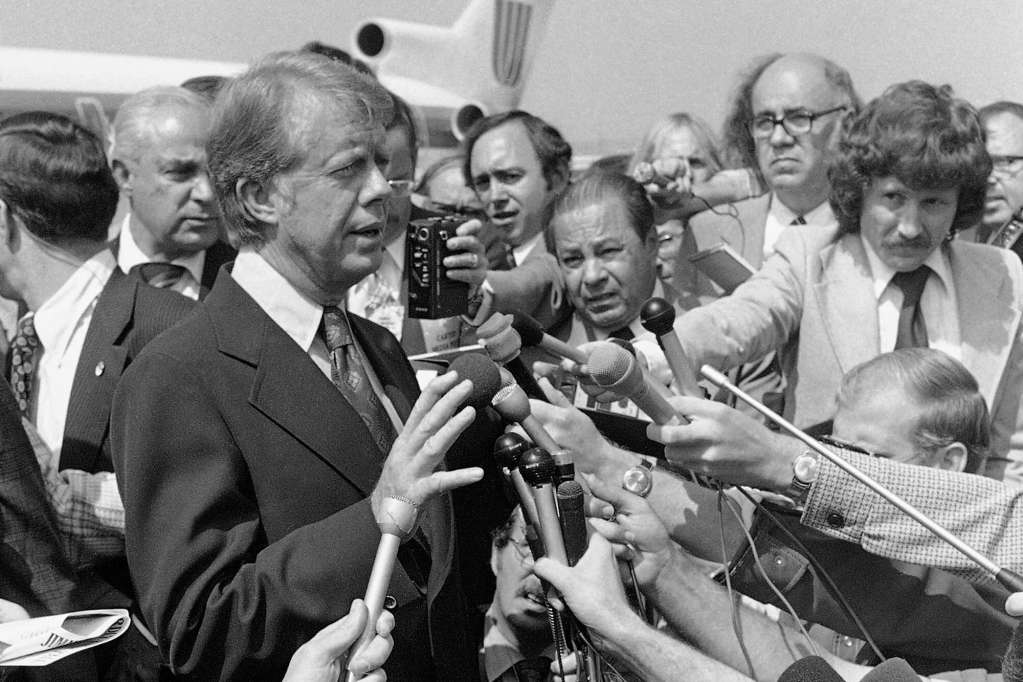 An older black and white photo of Jimmy Carter speaking to the press on an airport tarmac