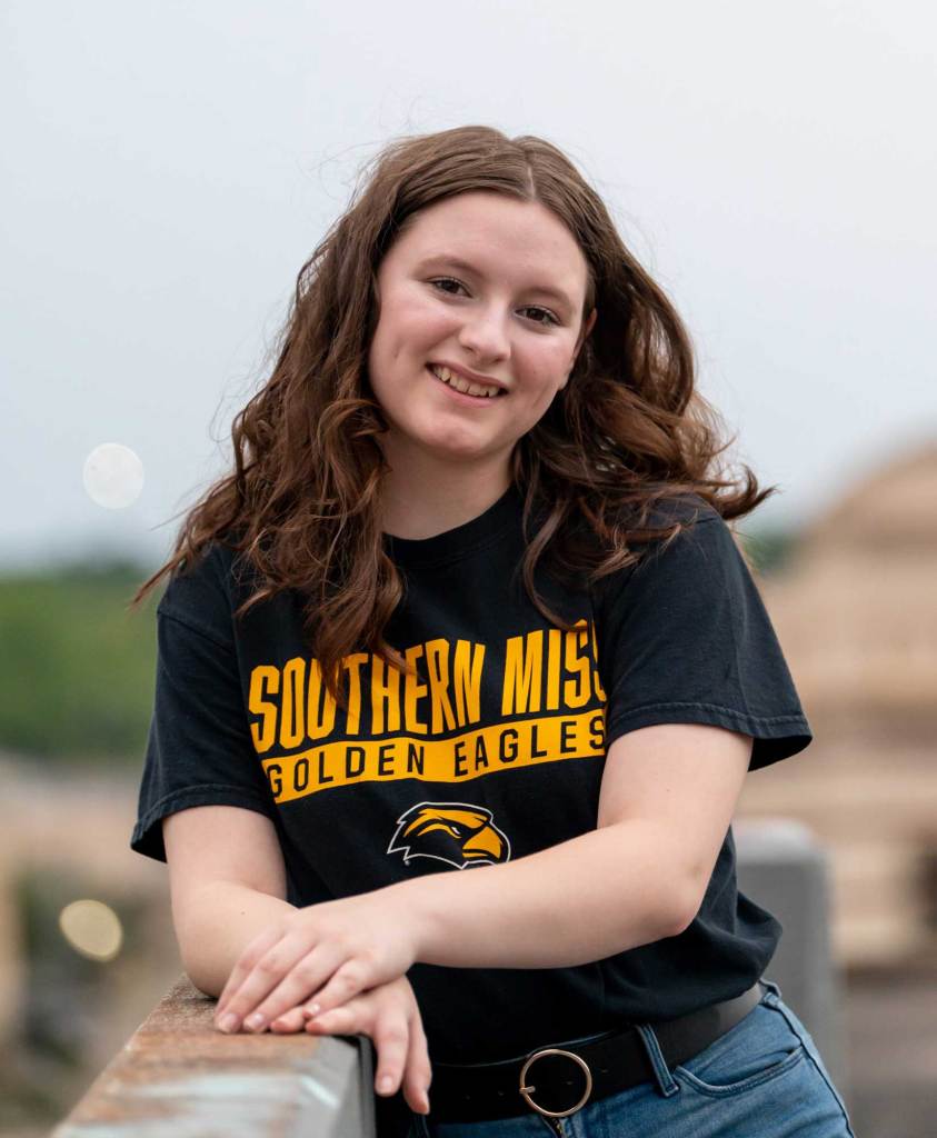 A woman wearing a black shirt that reads 'Southern Miss Golden Eagles' poses outside on a bridge