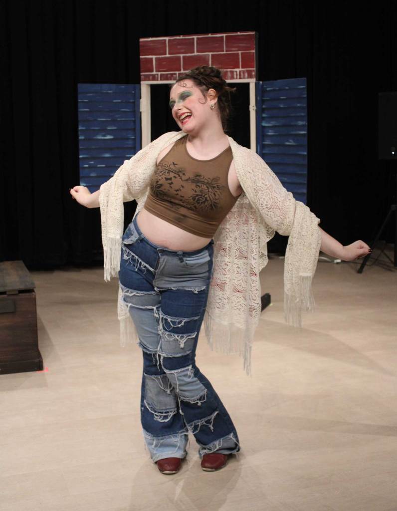 A woman wearing a lace shawl and jeans poses on a stage